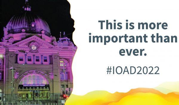 Flinders Street Station lit up with purple light. Text alongside reads: "This is more important than ever. #IOAD2022"