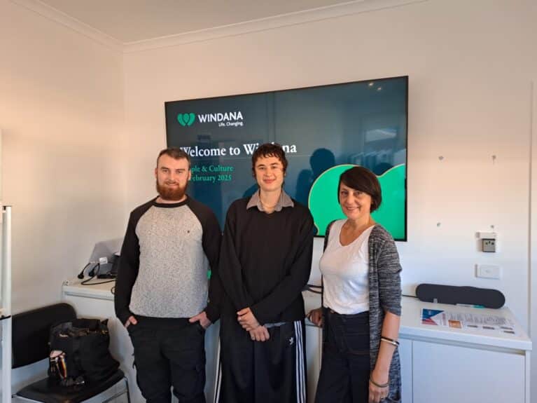 Three people stand in a meeting room, Windana Trainees Hamish, Millie and Mirella