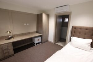 A room with a single bed, desk and wardrobe. A door is open to an ensuite bathroom